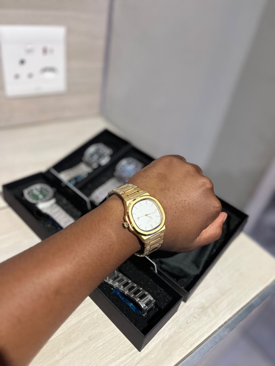 Gold-tone dress watch on wrist with watch tray in background — TIMAUNLIMITED.CO